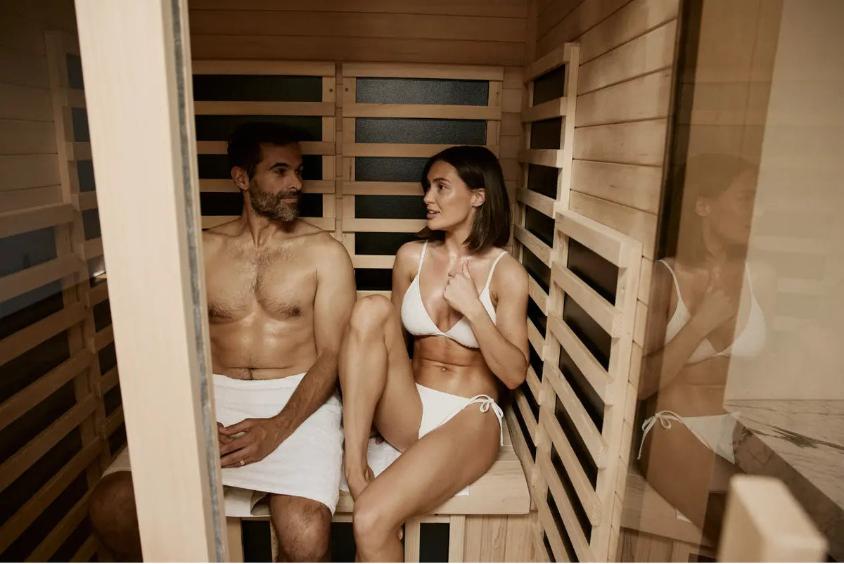 Two people in swimwear sitting inside a wooden sauna.
